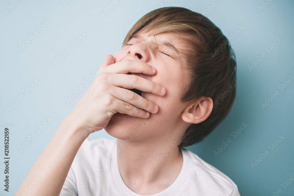 Boy yawns with his eyes closed, covering his mouth with his palm Boy yawns with his eyes closed, covering his mouth with his palm