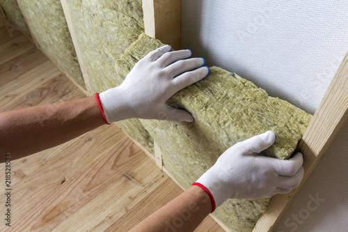 Close-up of worker hands in white gloves insulating rock wool insulation staff in wooden frame for future walls for cold barrier. Comfortable warm home, economy, construction and renovation concept.