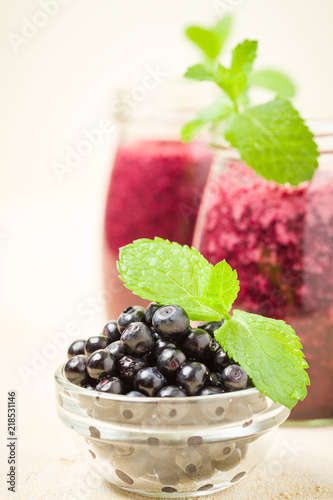 Blueberry smoothie decorated with fresh green mint leaves and raw ripe berries.