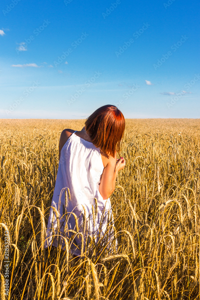 A young red-haired girl enjoys the beauty of a wheat field and a beautiful blue sky A young red-haired girl enjoys the beauty of a wheat field and a beautiful blue sky