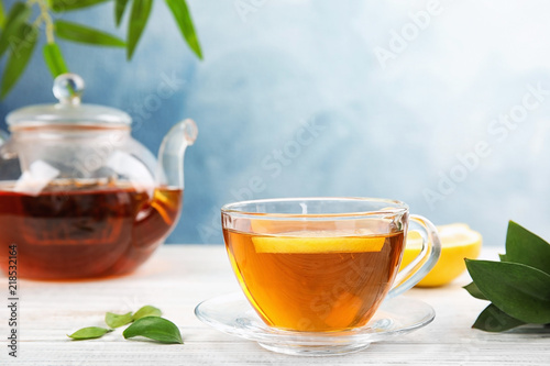 Glass cup and teapot with black tea on wooden table