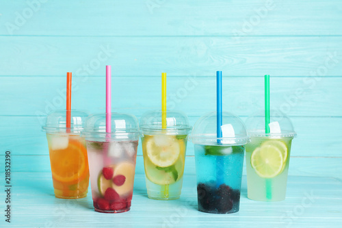 Fotografie, Tablou Plastic cups with lemonades on table against color background