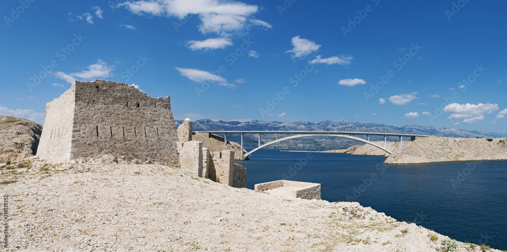 Croazia: vista panoramica delle rovine di una torre di guardia e del Paški Most, il ponte del 1968 che collega la Croazia con l'isola di Pago, la quinta isola più grande della costa croata