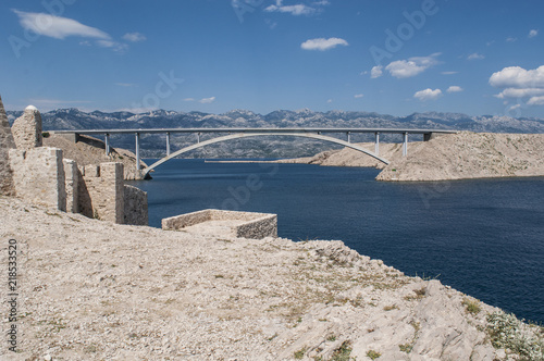Croazia: vista panoramica delle rovine di una torre di guardia e del Paški Most, il ponte del 1968 che collega la Croazia con l'isola di Pago, la quinta isola più grande della costa croata
