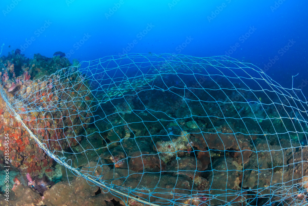 A huge abandoned ghost fishing net entangled over a large part of a  tropical coral reef Stock Photo