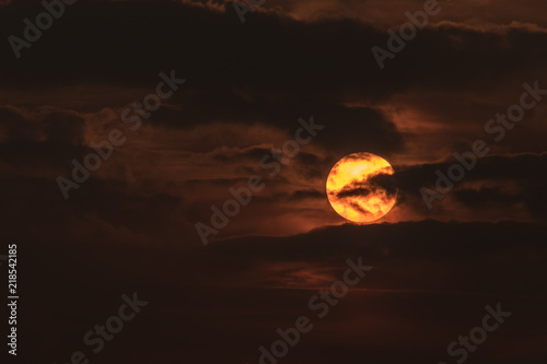 Clouds in front of sun during sunset in orange sky
