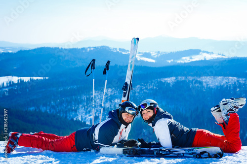 Hugging couple in ski masks lying on the snow with snowboards standing near photo