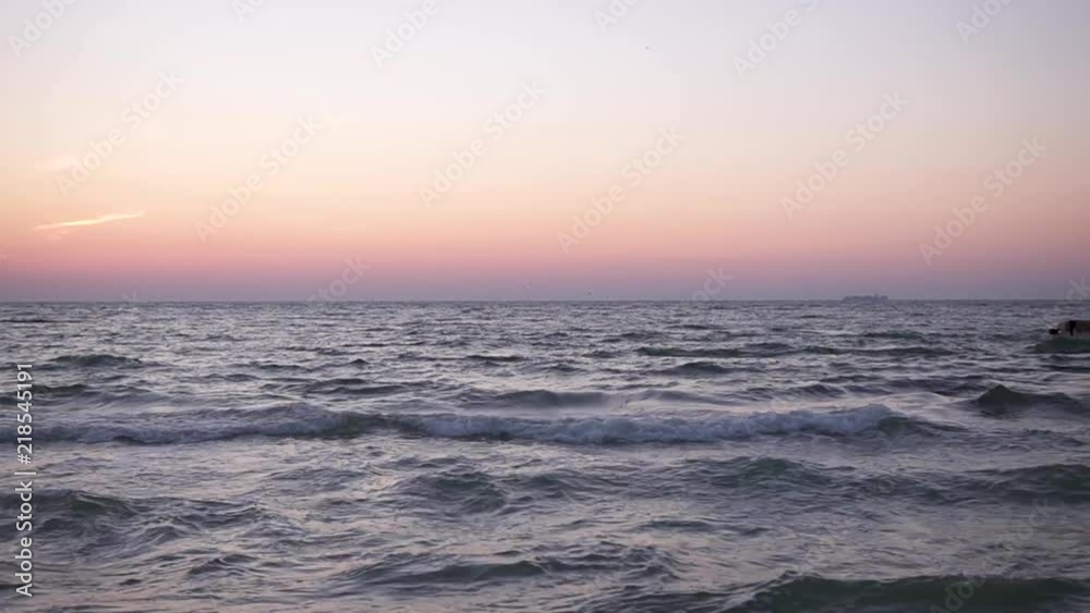 The lonely silhouette of a young girl in fluttering clothes is walking along the sea pier at dawn, against the rising sun The lonely silhouette of a young girl in fluttering clothes is walking along the sea pier at dawn, against the rising sun