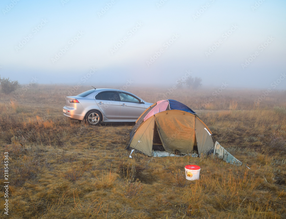 Car next to the tent. Fog at dawn.