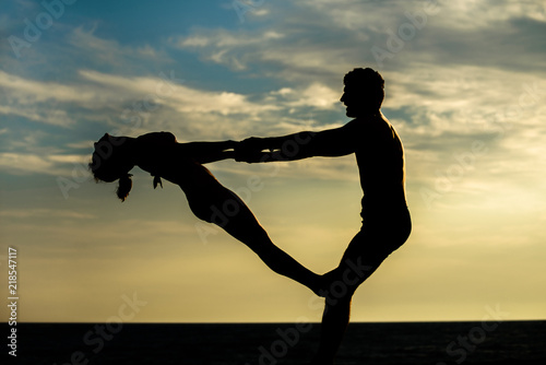 Couple practicing acro yoga on the beach with sunset. Acro yoga concept. Pair yoga. Yoga flexibility