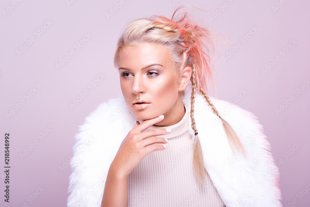 Gorgeous young woman in elegant winter fur coat, wearing makeup and braided hairstyle, posing against pink background. Studio lighting, retouched