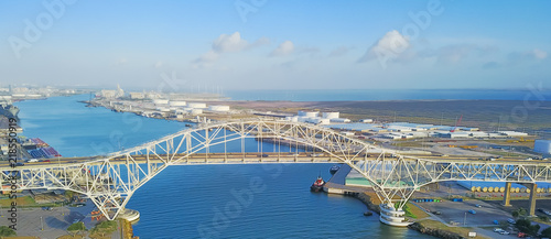 Panorama aerial view of Corpus Christi Harbor Bridge with row of oil tanks and wind turbines farm in distance. A through arch bridge crosses the Corpus Christi Ship Channel