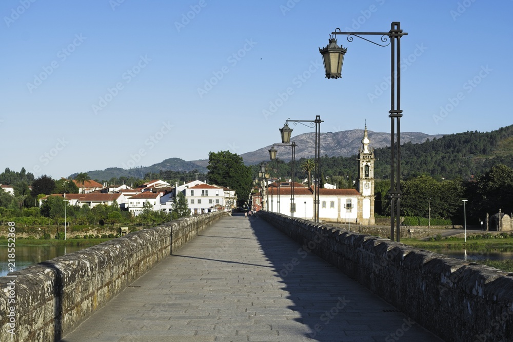 Roman bridge in Ponte de Lima, district of Viana do Castelo. Beautiful historic stone supported by the architecture of its arches. Typical old lamps in Portugal, and the Santo António da Torre church
