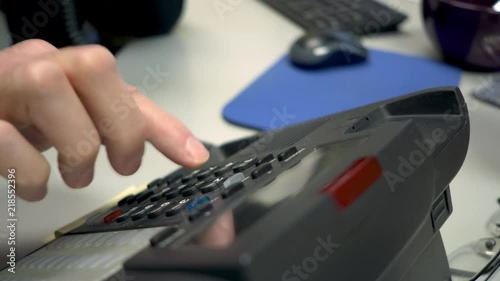 An office desk phone being used by a businessman to place a landline phone call.