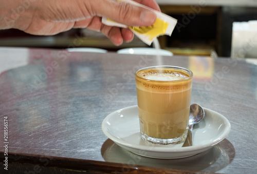 Male hand pouring sugar on a coffee.