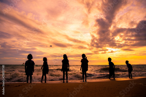 Silhouette children group enjoy playing sea waves on the beach in sunset with beautiful twilight sky