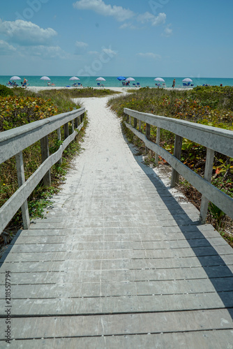 Fototapeta Naklejka Na Ścianę i Meble -  Dramatic vertical view of Wood Bridge looking toward a Sandy Ocean Beach with Colorful Umbrellas on a Sunny Day