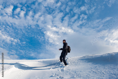 A man walks on the first snow, goes uphill in the snow against a dramatic winter sunset