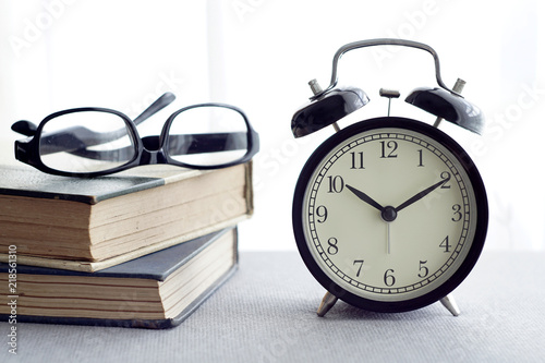 An alarm clock, spectacles and books over white curtain background