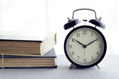 An alarm clock, spectacles and books over white curtain background