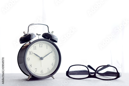 An alarm clock and a spectacles over white curtain background