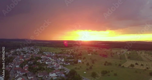 Dronevideo with view on the bloodsun. Look like orange glowing near to rainy thunder clouds with flashes and a village o the ground. photo