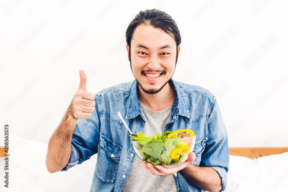 Young man eating organic healthy salad with vegetable in bowl on bed at home.diet food and healthy life concept Young man eating organic healthy salad with vegetable in bowl on bed at home.diet food and healthy life concept