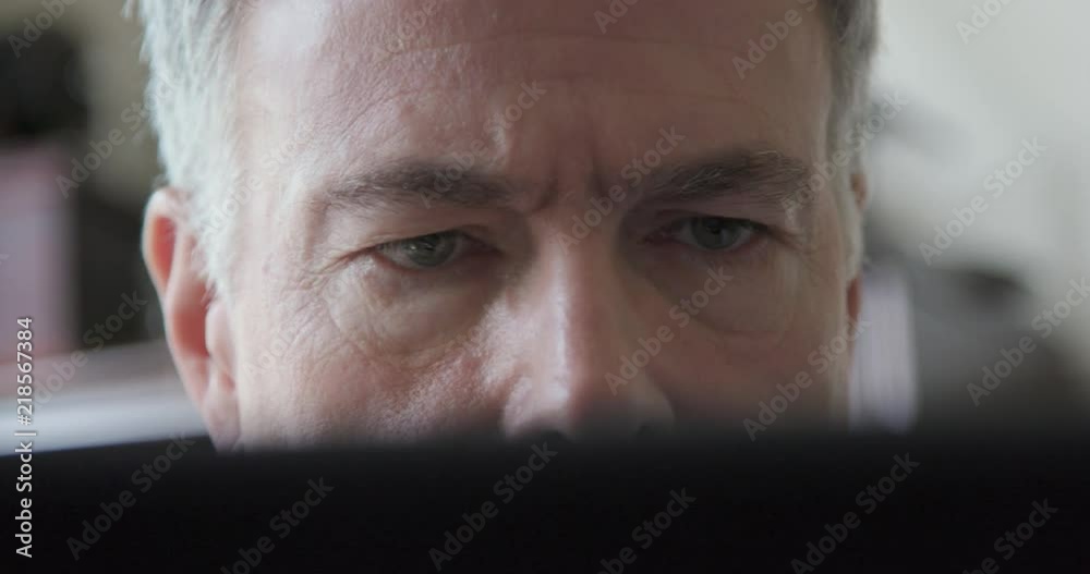 A mature man looking over a laptop leans forward to get a better look at the screen. A mature man looking over a laptop leans forward to get a better look at the screen.