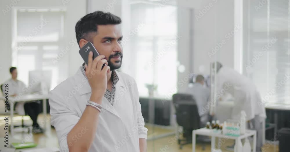 Cardiologist talking on phone with patient. Stands on background of working colleagues in center of cardiology and study of cardiovascular system Cardiologist talking on phone with patient. Stands on background of working colleagues in center of cardiology and study of cardiovascular system