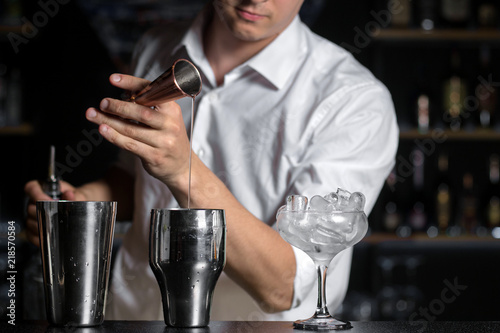 Bartender mixologist is pouring sugar syrup from a jigger into shaker.