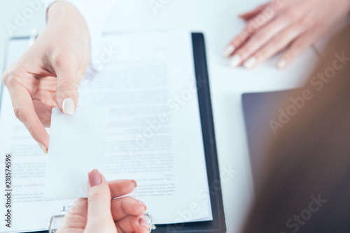 Female physician hand give white blank calling card to businesswoman closeup in office.