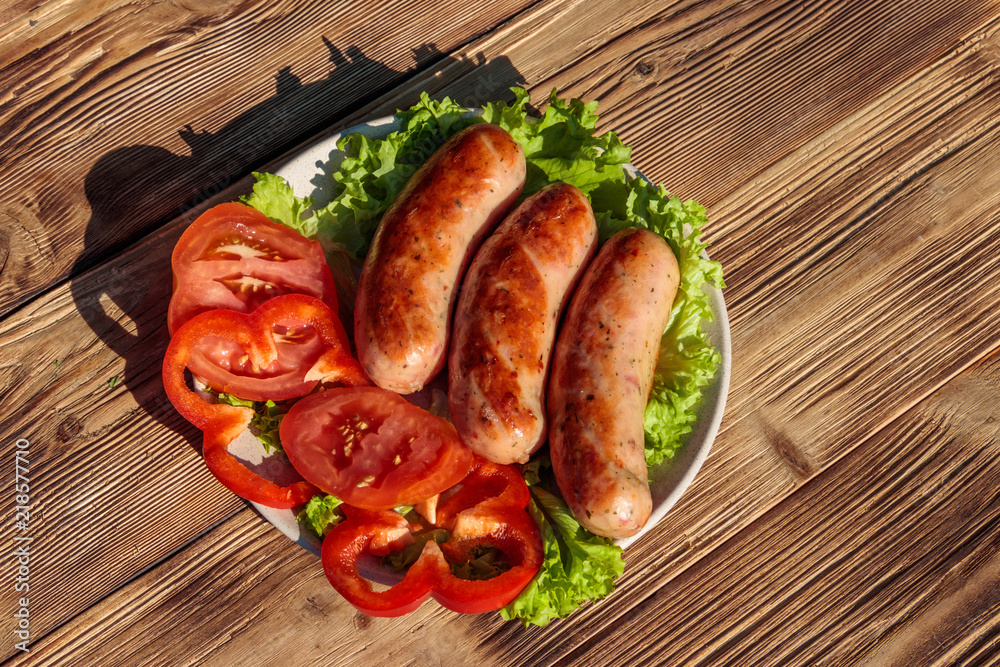 Grilled sausages with fresh vegetables on wooden table