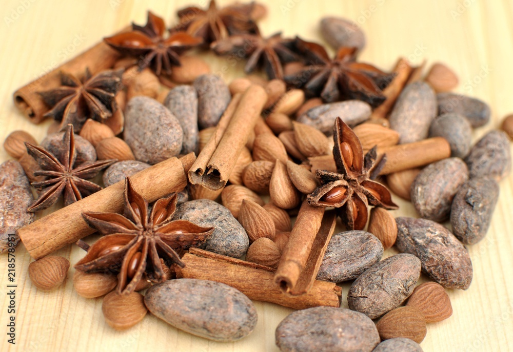 Top side view of ingredients for chocolate, cocoa beans, cinnamon, anise, apricot beans on natural wood background, selective focus Top side view of ingredients for chocolate, cocoa beans, cinnamon, anise, apricot beans on natural wood background, selective focus
