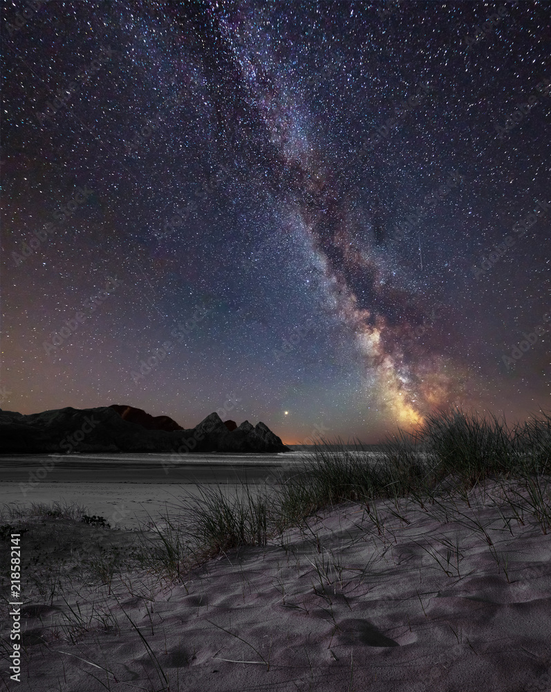 Vibrant Milky Way composite image over landscape of yellow sandy beach Three Cliffs bay