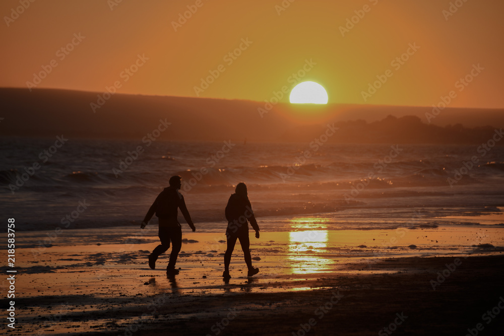 2 people walking through a sunset at the beach