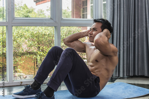 Muscular male exercising doing sit up on blue yoga mad