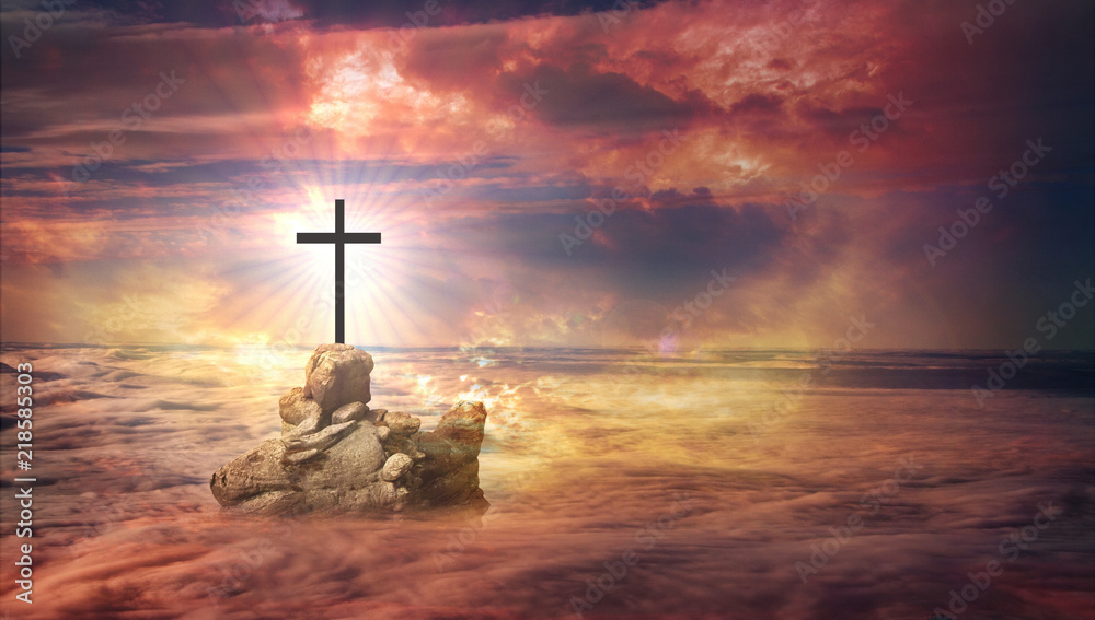 A cross on a lonely rock protruding above the clouds - fog, in the distance you can see the rising sunflowers.