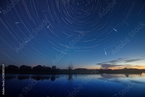 Blue sky with Star trails and falling stars - perseids reflected in the water