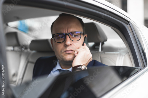 young successful businessman talking on the phone sitting in the back seat of an elite car, talks and business meetings