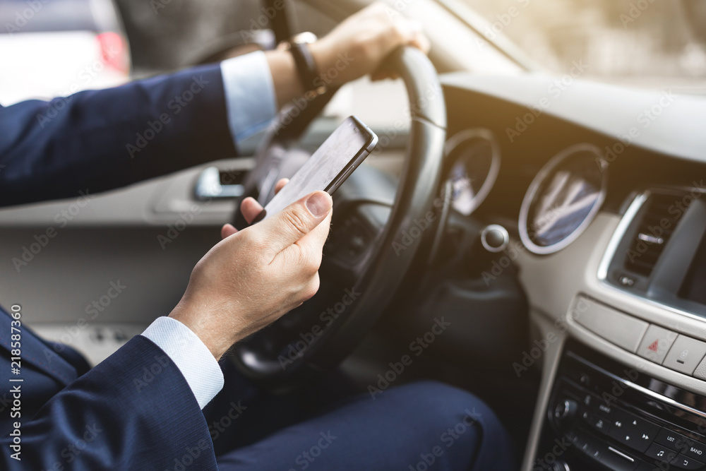 a businessman driving a prestigious car holds a mobile phone in his hand. Hasty life