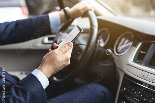 a businessman driving a prestigious car holds a mobile phone in his hand. Hasty life