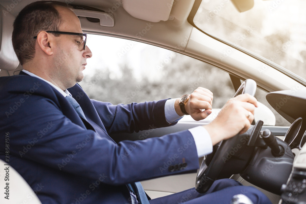 a businessman driving a prestigious car holds a mobile phone in his hand. Hasty life