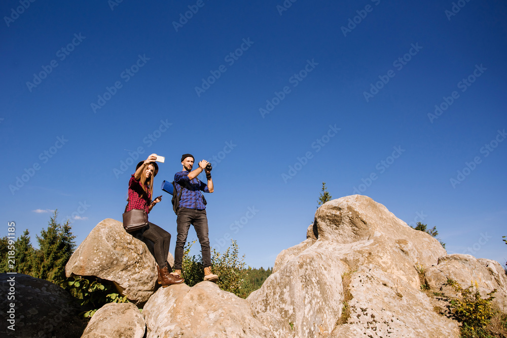 A traveler couple standing together on the rocks at the mountains over the blue sky background