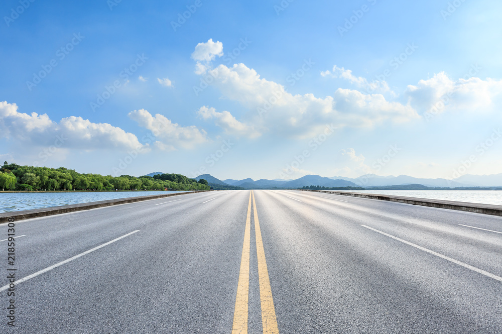 Fototapeta premium Empty asphalt road and lake with mountains on a sunny day