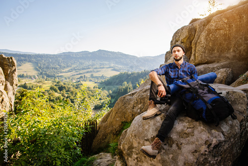 Tired man traveler sitting on the rocks and holding a backpack