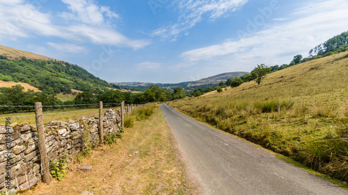 Typical landscape of Brecon Beacons National Park with mountians, trees and stone walls along the small roads.