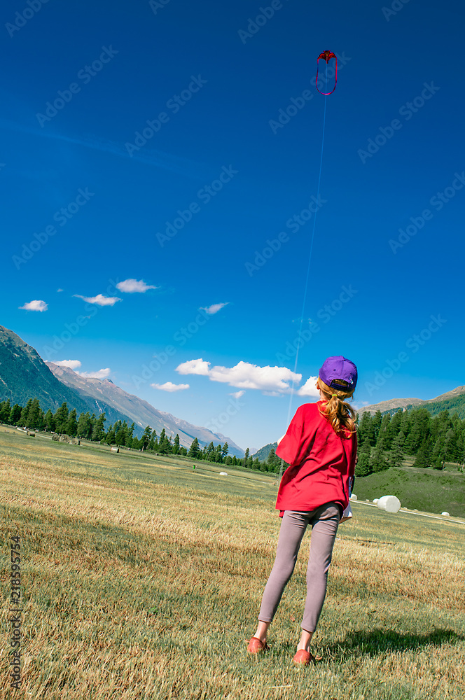 Obraz premium Little girl plays with her kite in large mountain meadows