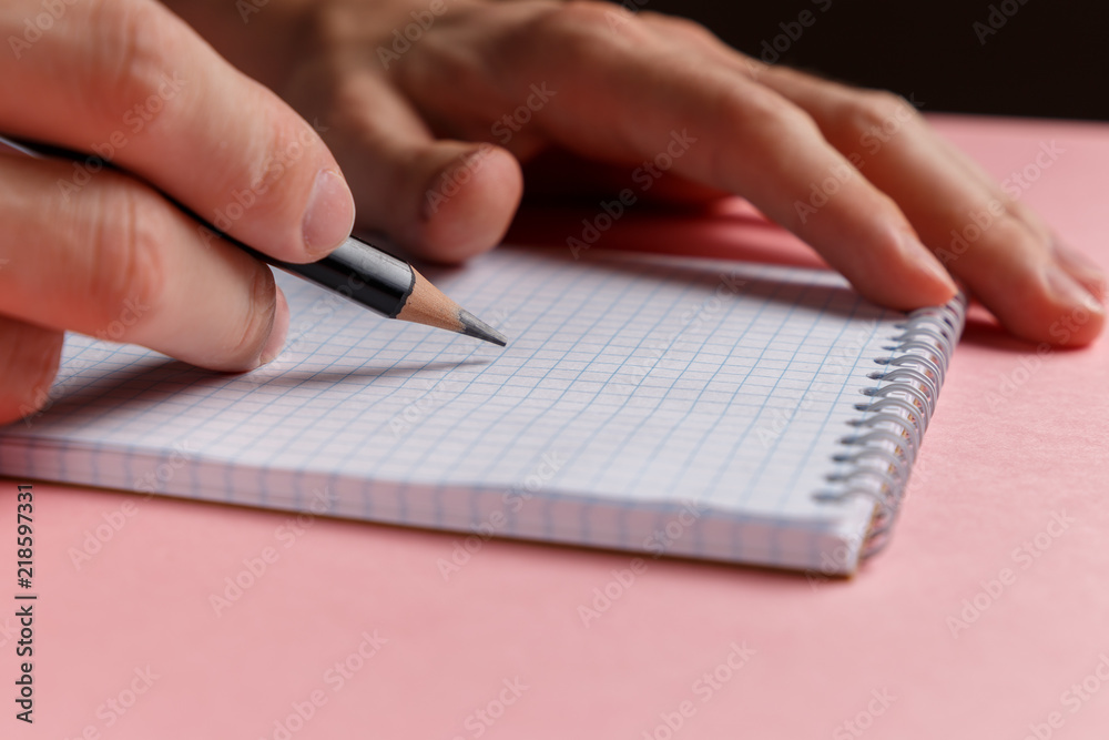 Man's hands holding pencil and spiral notepad as mockup for your design. Pink background. Pastel background. Back to school and education concept Man's hands holding pencil and spiral notepad as mockup for your design. Pink background. Pastel background. Back to school and education concept