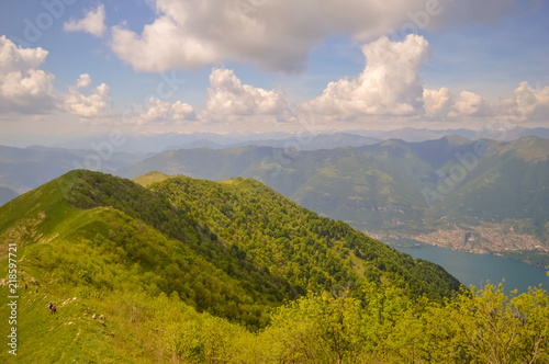 A summer day landscape view of a green valley with a river and green mountains and a blue sky and a small coastal city visible