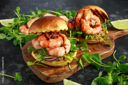 Healthy Tasty prawn grilled burger with pea shoots and sweet chilli dip served on wooden board with lime wedges